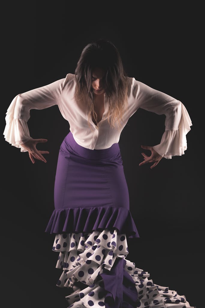 Elegant flamenco dancer in a studio, posing with purple skirt and ruffled sleeves.